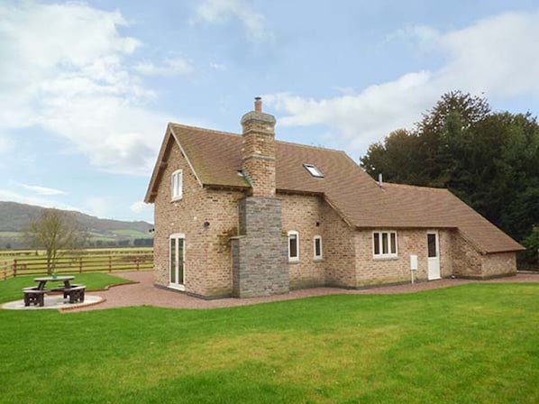 A stone building with a pitched roof, a chimney, and a small porch with a table and chairs.
