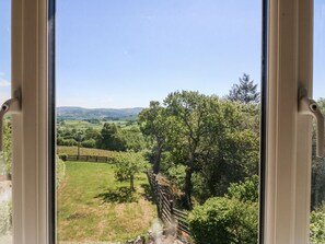 A view through a window with a wooden fence and trees. - Holly Cottage, Conwy (Conwy)