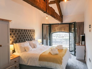 A bedroom with a tufted headboard, a bed with white linens, a bedside table with a lamp, and a view through a glass door. - Flying Scotsman @ Engine Shed, Whitby (Whitby)