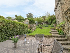 A patio with a table and chairs, a glass of wine, and a vase of flowers. - Holly Cottage, Winster (Matlock)