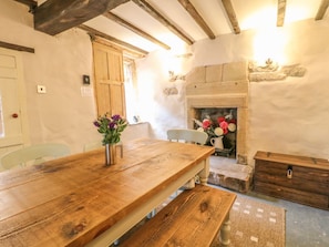 A rustic room with a wooden table, a fireplace, and stone walls. - Holly Cottage, Winster (Matlock)