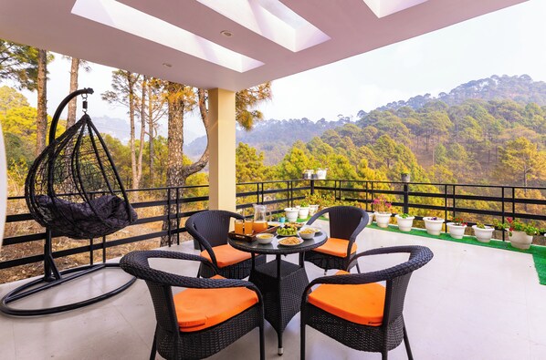 A balcony with wicker furniture, a hanging chair, and potted plants. - ELIVAAS The Nakshatra Serene 3BHK Villa (Sukha)