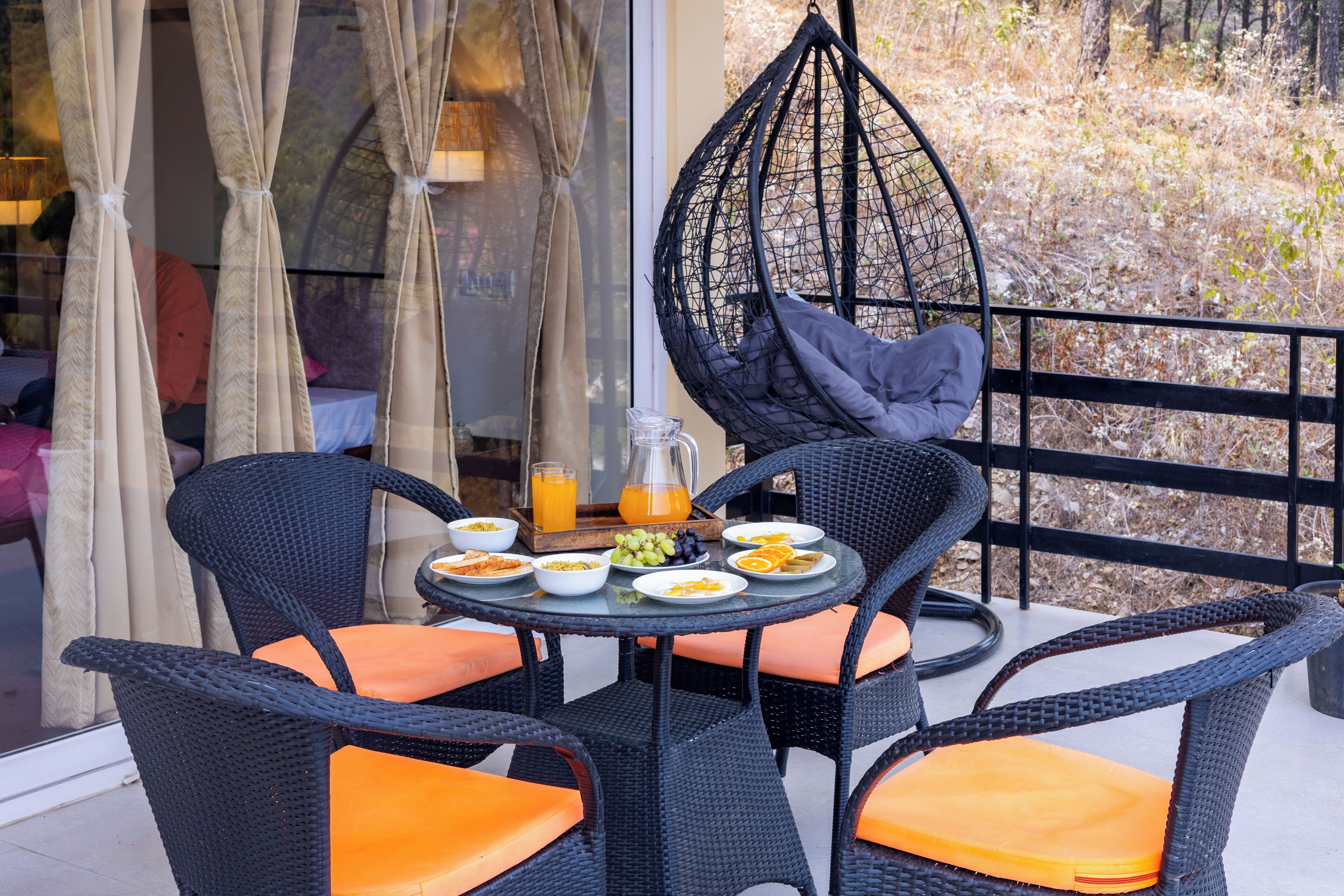 A dining area with wicker chairs, a round table, and a hanging chair.