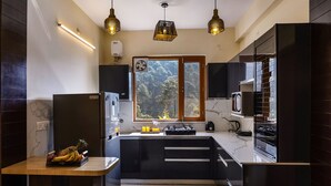 A modern kitchen with a central island, built-in appliances, and a large window with a view of trees. - ELIVAAS The Nakshatra Serene 3BHK Villa (Sukha)