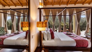 A four-poster bed with a wooden ceiling, a bedside table with a lamp, and a view of the outdoors through large windows. - ELIVAAS The Nakshatra Serene 3BHK Villa (Sukha)