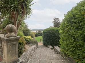 A stone pathway leading to a view of a landscape with a hedge on the right and a palm tree on the left. - The Croft, Peterchurch (Hereford)