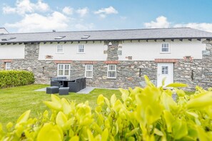 A two-story stone building with a flat roof, multiple windows, and a patio area with outdoor furniture. - Sgubor: Charming Retreat in Cleifiog Fawr (Holyhead)