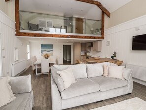 A spacious living area with a high ceiling, a dining table, a sofa, and a kitchen area. - Sgubor: Charming Retreat in Cleifiog Fawr (Holyhead)