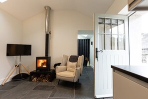 A cozy living room with a fireplace, a comfortable armchair, a television, and a door leading to another room.