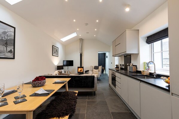 A modern interior with a dining area, sofa, fireplace, kitchen, and large windows.