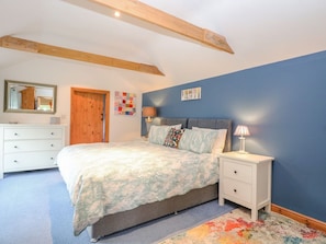 A bedroom with a bed, a nightstand, a dresser, a mirror, a door, and a blue wall. - The Lodge: A Serene Retreat (Norwich)