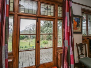 A room with a large wooden-framed window, a wooden deck, and a chair. - Hill Brow, Hatton, Shropshire (Church Stretton)