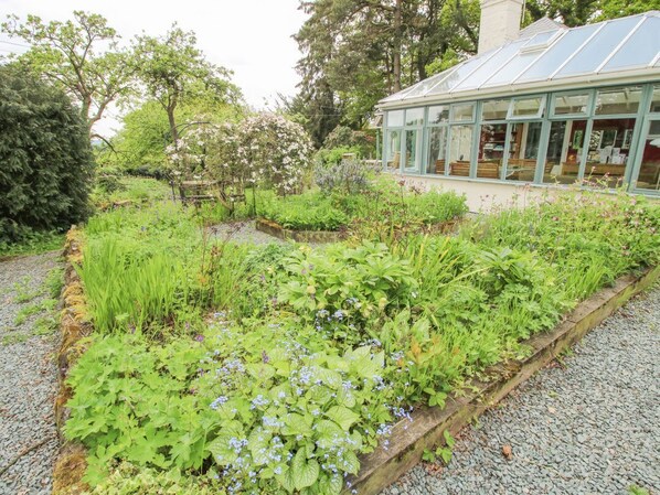 A greenhouse with a glass roof, surrounded by a garden with various plants and flowers. - Hill Brow, Hatton, Shropshire (Church Stretton)