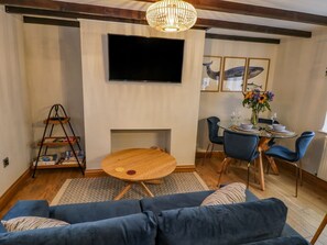 Un soggiorno con un divano blu, un tavolino rotondo in legno, una TV a parete e un'area pranzo con sedie blu e un tavolino.