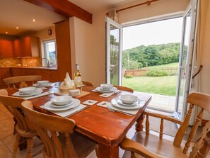 A dining area with a table set for six, a bottle of wine, and a view of a garden through a glass door. - Wayside, North Yorkshire 3 bed (Whitby)