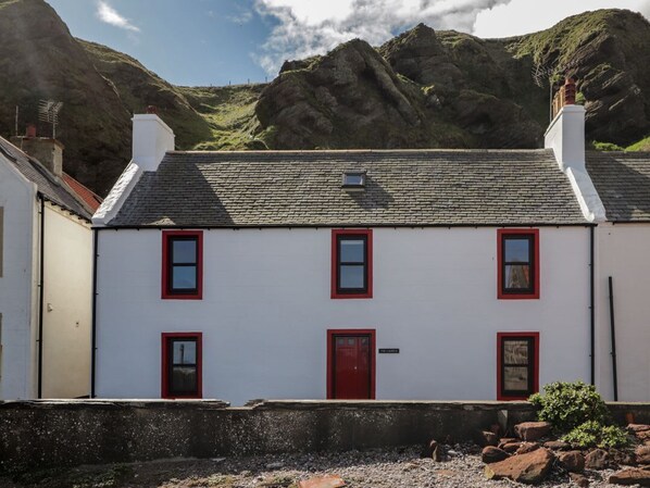 A white building with red doors and windows, set against a mountainous backdrop.