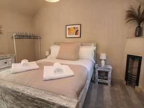 Ein Schlafzimmer mit einem Bett, zwei Nachttischen, einem an der Wand befestigten Handtuchhalter, einem gerahmten Bild und einer Vase mit Trockenpflanzen.