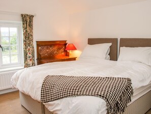 Ein Schlafzimmer mit einem Bett, einem Nachttisch mit Lampe, einem Fenster mit Vorhängen und Blick auf Grünfläche.