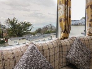Ein Fenster mit Blick auf Häuser und Bäume, ein Fensterladen und ein Sofa mit Kissen.