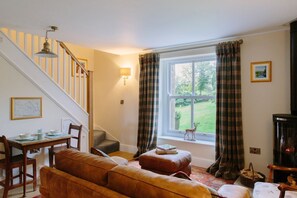 Ein Wohnzimmer mit einer Couch, einem Tisch mit Stühlen, einem Kamin, einer Treppe und einem Fenster mit Vorhängen.