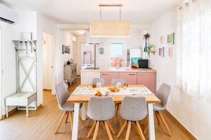 Un comedor con mesa de madera, sillas grises, una lámpara colgante y una cocina al fondo.