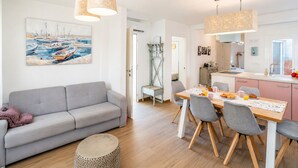 Un salon moderne avec un canapé gris, une table à manger et des chaises, et un tableau représentant des bateaux accroché au mur.