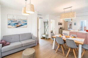 A modern living room with a gray sofa, dining table with chairs, and a painting of boats on the wall. - Cubo's Casa Nerja Roof Terrace / near beach / air conditioning / free wifi (Nerja)