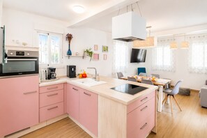 A modern kitchen with pink cabinets, a built-in oven, and a dining area with a table and chairs. - Cubo's Casa Nerja Roof Terrace / near beach / air conditioning / free wifi (Nerja)