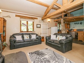 Ein Wohnzimmer mit zwei Ledersofas, einem gemusterten Teppich, Holzbalken, einer Küche im Hintergrund und einer Steinwand.