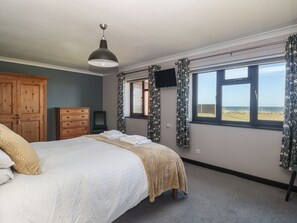 Ein Schlafzimmer mit einem Bett, einem Holzschrank, einem Fernseher und einem Fenster mit Vorhängen.