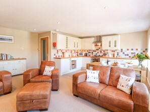 A modern kitchen with white cabinets, a central island, and a dining area with a brown leather sofa set. - Crab Corner, Wells-Next-The-Sea (Wells-next-the-Sea)
