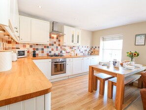 A modern kitchen with white cabinets, a wooden countertop, and a dining area with a wooden table and benches. - Crab Corner, Wells-Next-The-Sea (Wells-next-the-Sea)
