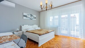 Une chambre à coucher comprenant un lit, une table de chevet, une lampe, une chaise et une fenêtre avec des rideaux légers.