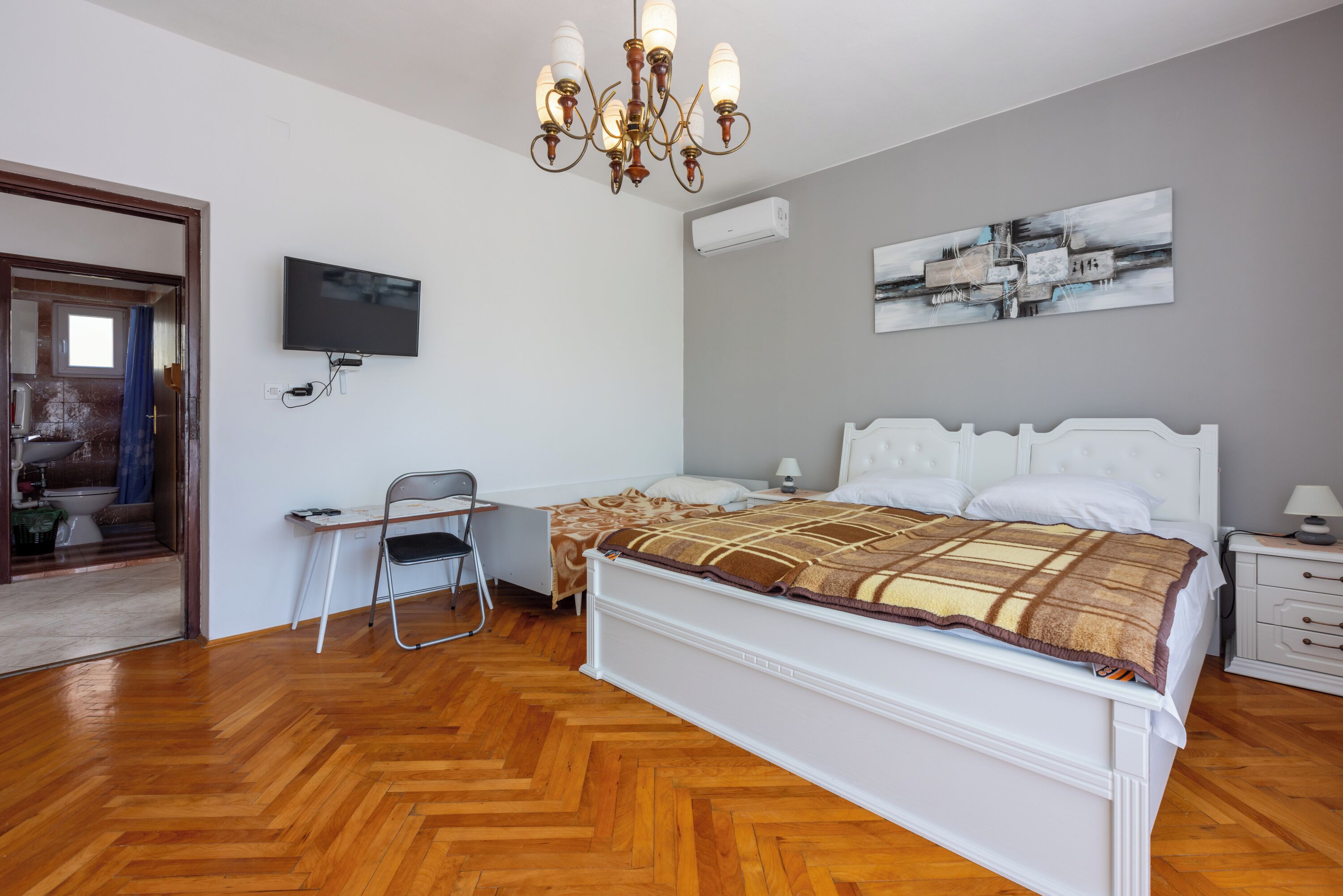 Quarto com cama, mesa de cabeceira, cadeira, televisão, obra de arte e um candelabro.