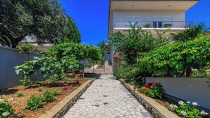 Un chemin de pierre mène à un bâtiment doté d’un balcon, qui est entouré de verdure et de plantes.