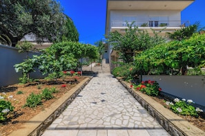 A stone pathway leading to a building with a balcony, surrounded by greenery and plants. - Spacious apartment for 6 people with balcony and sea view in Dramalj (Dramalj)