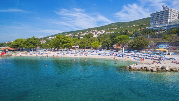 Une plage avec une eau claire, des parasols et des gens.