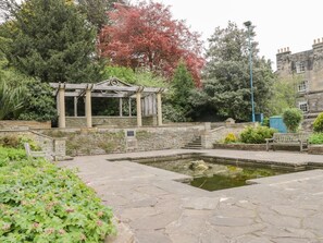 A stone fountain with a wooden pergola, surrounded by greenery and a stone wall. - Charming Park View Apartment in Whitby (Whitby)