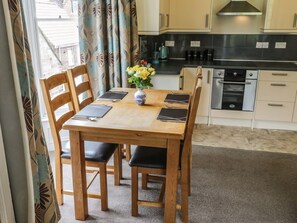 A dining area with a wooden table and chairs, a vase with flowers, and a kitchen in the background. - Charming Park View Apartment in Whitby (Whitby)