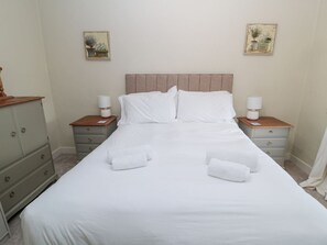 Un lit bien fait, avec du linge de lit blanc, deux tables de chevet avec des lampes et une commode à tiroirs.