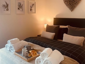 A hotel room with a bed, pillows, a tray with towels, a teapot, and croissants. - Angel's Cottage, Tideswell. TV (Buxton)