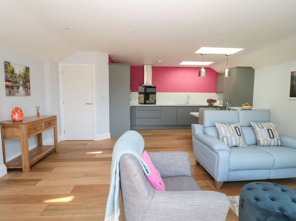 A modern living room with a sofa, ottoman, and a dining area with a table and chairs. - 3 The Paddock, Beadnell (Chathill)
