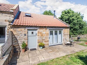 A stone house with a tiled roof, a small porch, and a grill outside.