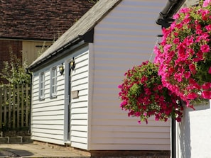 A white building with a sloped roof and a hanging flower basket with pink flowers. - White Hart Stables, Catsfield (Battle)