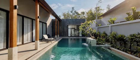 A modern pool area with clear water, wooden pillars, and a lounge chair.