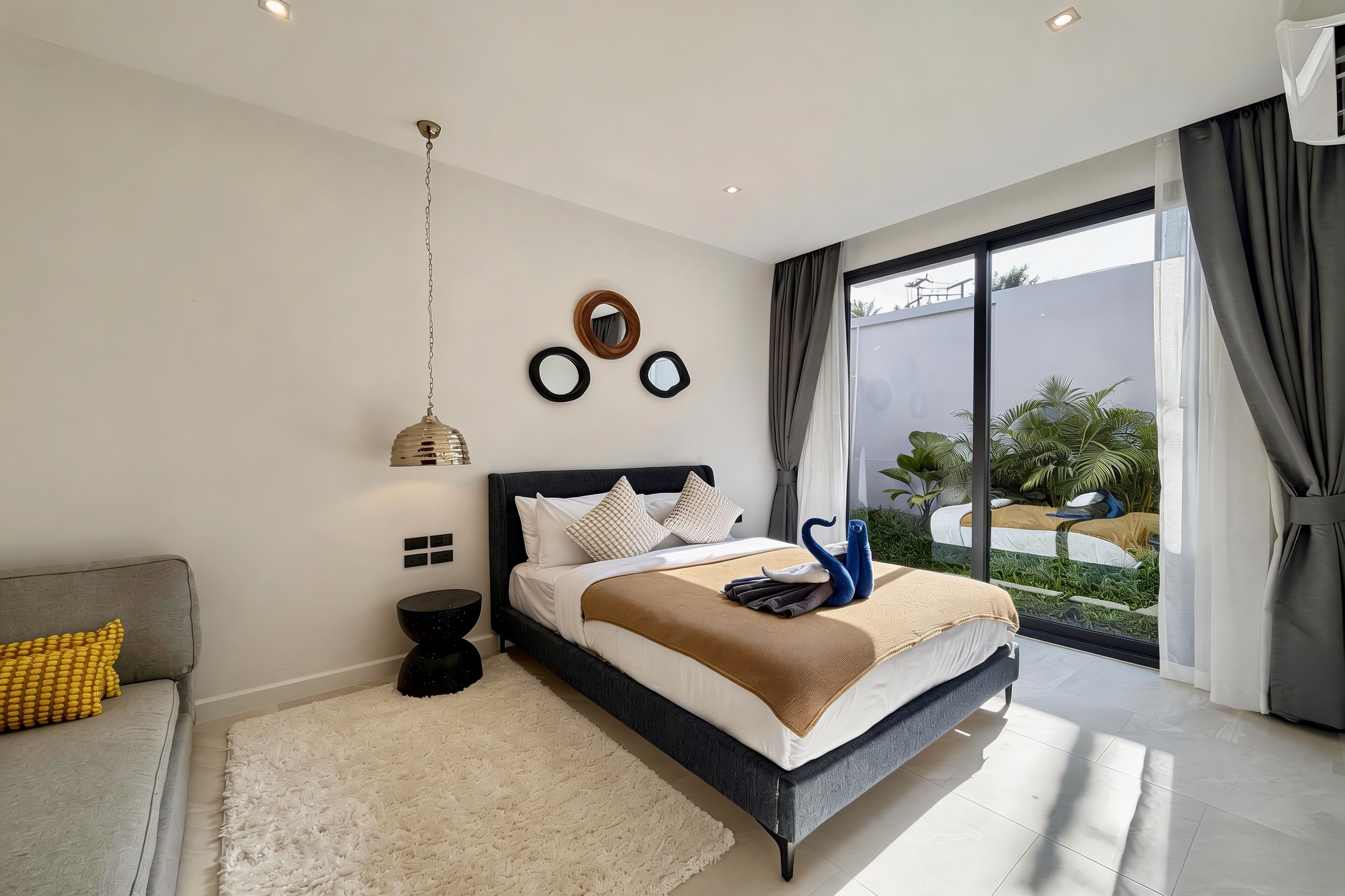 Une chambre moderne avec un grand lit, un canapé, un luminaire suspendu et une vue sur un balcon.