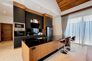 A modern kitchen with a central island, built-in appliances, and a dining area with bar stools. - Bougainvillea Luxury Pool Villas (Choeng Thale)