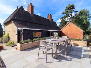 A house with a patio, a table with chairs, and a garden. - The Alms House East is in Forthampton (Gloucester)