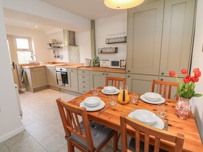 A kitchen with a dining table set for four, a microwave, and a vase with flowers. - The Cottage Bradwell, Bradwell (Hope Valley)