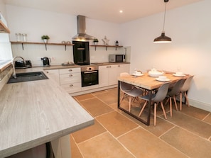 A modern kitchen with a wooden countertop, built-in oven, microwave, and a dining area with a wooden table and chairs. - Canny Cottage: A Pet-Friendly Retreat (Belford)